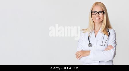 Professionelle Ärztin lächelt selbstbewusst mit überkreuzten Armen in einer klinischen Umgebung Stockfoto
