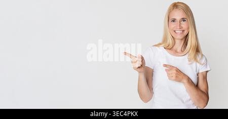 Die Lächelnde Frau Mit Weißem Hemd Zeigt Mit Beiden Händen In Richtung Leerraum Drinnen Stockfoto