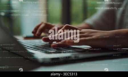 Ein Programmierer bewegt sich auf einem Laptop in einer hellen Büroumgebung, umgeben von einem abstrakten Code-Overlay, das die dynamische Welt der Software veranschaulicht Stockfoto