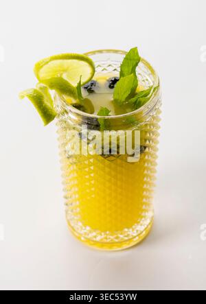 Erfrischendes Zitrusgetränk mit Orangensaft, Limettenscheiben, Heidelbeeren und frischen grünen Minzblättern, serviert in strukturiertem Glas, isoliert auf weißem Hintergrund Stockfoto