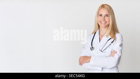 Selbstbewusste Ärztin stehend mit überkreuzten Armen in einer professionellen Umgebung mit einem warmen Lächeln Stockfoto