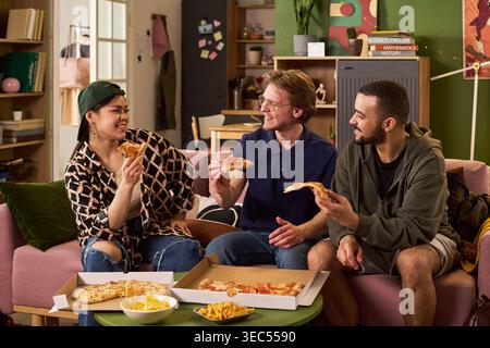 Multiethnische Studenten teilen sich Pizza und unterhalten sich in der Wohnung, zeigen Freundschaft und Campus-Lebensstil. Ideal für Bildungsmarketing, Studentenwohnheime und Kampagnen zur Jugendgemeinschaft Stockfoto