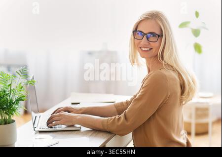 Frau, die in einem hellen, modernen Home Office mit Pflanzen und natürlichem Licht an einem Laptop arbeitet Stockfoto