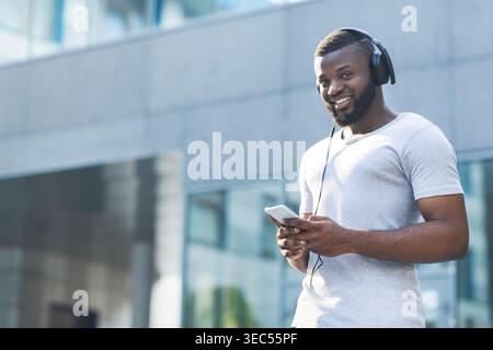 Junger Mann, der tagsüber Musik genießt, während er vor einem modernen Gebäude steht Stockfoto