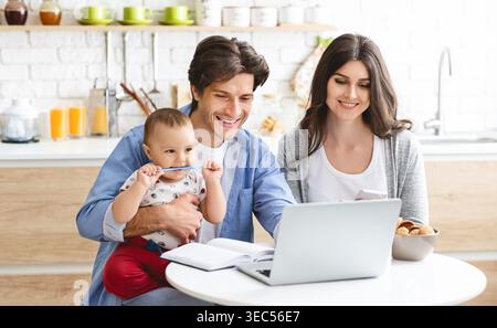 Die Familie genießt eine gute gemeinsame Zeit, während sie ein Notebook in einer hellen, modernen Küche verwendet Stockfoto