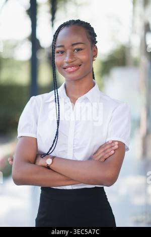 Selbstbewusste junge schwarze Geschäftsfrau, die draußen steht, Arme gekreuzt und lächelnd. Professionelles Porträt, Führung, Karriereerfolg, Corporate ide Stockfoto