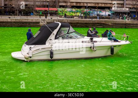 In Chicago versammeln sich Menschen, um den St. Patricks Day zu feiern, während der Fluss grün wird. Ein Boot fährt durch und trägt zur lebhaften Atmosphäre der Veranstaltung bei. Stockfoto