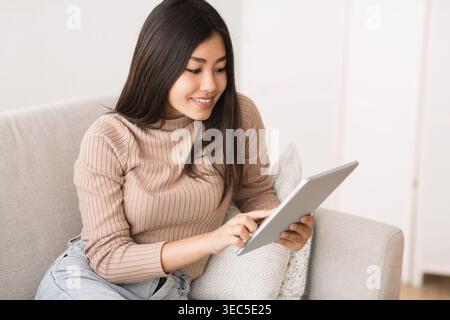 Junge Frau, die sich zu Hause mit digitalen Aktivitäten beschäftigt, während sie sich auf einem Sofa entspannt Stockfoto