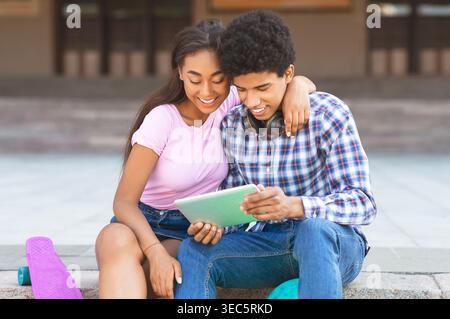 Junges Paar genießt die gemeinsame Zeit, während es sich ein Tablet in einer lebhaften Outdoor-Umgebung ansieht Stockfoto