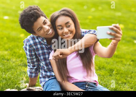 Ein Paar macht ein Selfie, während er an einem sonnigen Tag auf dem Gras sitzt Stockfoto