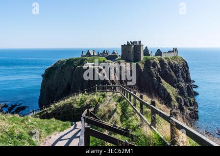 Die Ruinen von Dunnottar Castle liegen auf einer dramatischen Klippe über der Nordsee in der Nähe von Stonehaven in Schottland, mit einem malerischen Pfad und einem hölzernen Zaun, der zu Ihnen führt Stockfoto