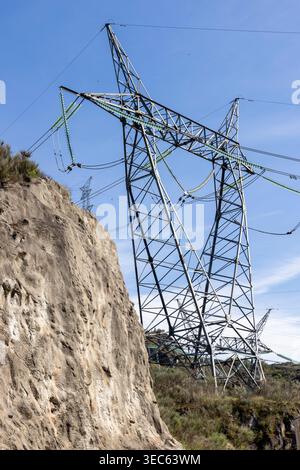 Elektrischer Pylon aus Metall, der Hochspannungsleitungen unterstützt und Energie in einer natürlichen, rauen Umgebung unter blauem Himmel überträgt Stockfoto
