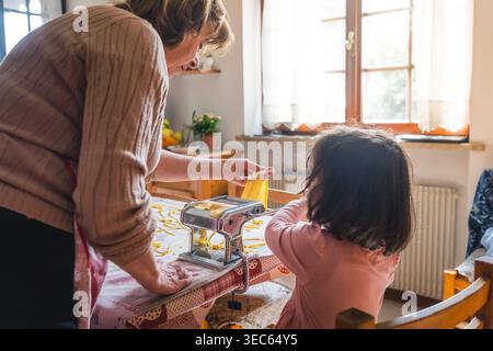italienerin mit Enkelin, die frische, handgemachte Tagliatelle-Pasta mit einer Hand-Pasta-Maschine herstellt, Oma mit Kindern macht Aktivitäten Stockfoto