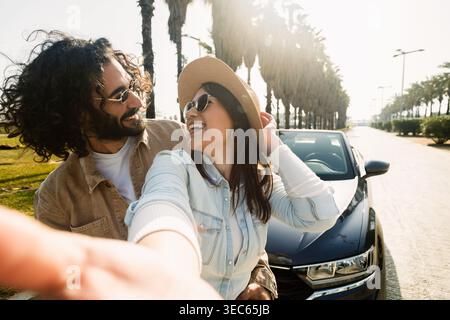 Ein junges Paar, das Selfie in der Nähe eines Cabrios macht, an sonnigem Tag Stockfoto