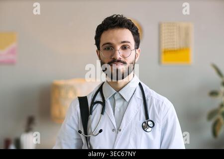 Porträt eines jungen erwachsenen kaukasischen Arztes, der in der Klinik steht, Stethoskop trägt und in die Kamera blickt, Vertrauen und Professionalität vermittelt Stockfoto