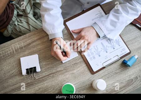Overhead-Aufnahme des verschreibungspflichtigen Arztes neben Patientenakte und Inhalator während der Sprechstunde Stockfoto