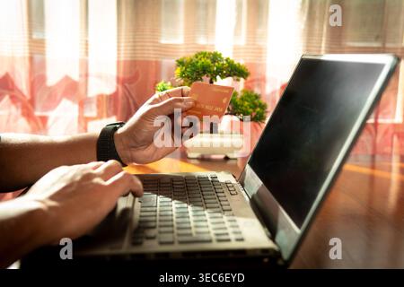 Mann mit orangefarbener Kreditkarte während der Nutzung des Laptops für Online-Zahlungen Stockfoto