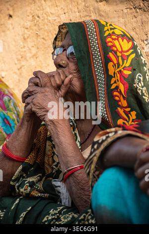 Nahaufnahme einer älteren Indianerin mit Brille, die ihr Kinn auf ihren gefalteten Händen in Bihar, Indien, mit nachdenklichem Ausdruck und verwittertem Featur Stockfoto