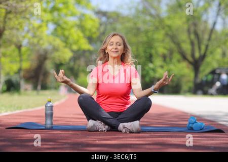 Seniorin meditiert in einer Lotuspose auf einer Yogamatte im Park Stockfoto