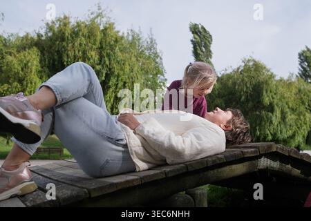 Mutterschaft Momente: Glückliche Mutter und Tochter, die zusammen auf einer Holzbrücke im Park entspannen Stockfoto