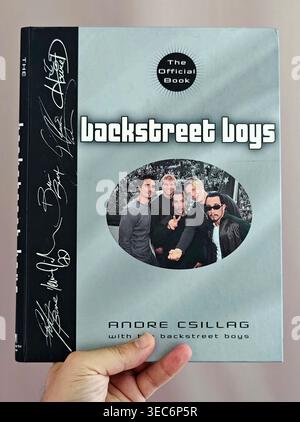 Hand hält das Buch „Backstreet Boys: The Official Book“ von Andre Csillag mit Faksimile-Signaturen und Bandporträt auf silbernem Cover. Stockfoto