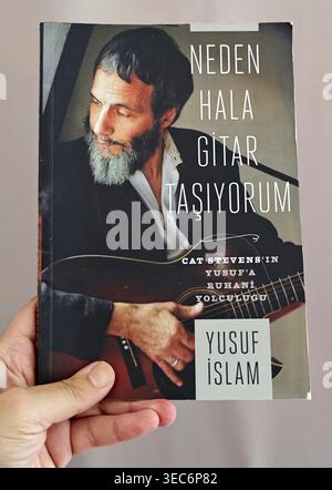Hand hält das Buch „Neden Hala Gitar Taşıyorum“ von Yusuf Islam (Cat Stevens) mit einem Porträt des Musikers, der eine Akustikgitarre auf Th hält Stockfoto
