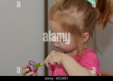 Seitenansicht von Kleinkinder-Mädchen-Malerei mit Pinsel und farbenfroher Farbe, fokussierte kreative Aktivität zu Hause, Kinderentwicklungs- und Lernkonzept, natürliches l Stockfoto