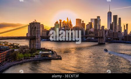 Die Brooklyn Bridge erstreckt sich über den East River und verbindet Manhattan und Brooklyn bei Sonnenuntergang. Wolkenkratzer bilden eine atemberaubende Kulisse. Stockfoto