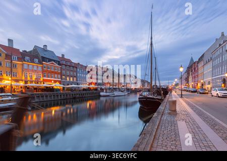 Ruhige Uferpromenade von Nyhavn bei Sonnenaufgang mit vertäuten Booten, ruhigen Kanalspiegeln und sanftem Morgenlicht in Kopenhagen, Dänemark. Stockfoto