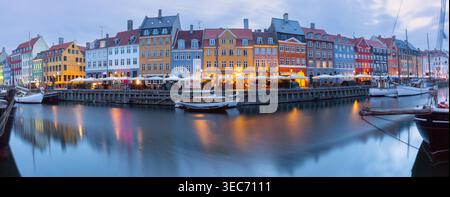 Ruhige Uferpromenade von Nyhavn bei Sonnenaufgang mit vertäuten Booten, ruhigen Kanalspiegeln und sanftem Morgenlicht in Kopenhagen, Dänemark. Stockfoto