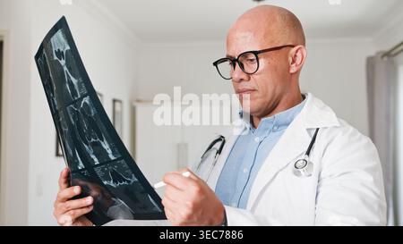 Erfahrener Arzt, der das medizinische Röntgenbild in der Klinik mit Stethoskop und Brille überprüft Stockfoto