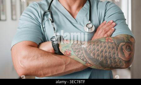 Tätowierter Arzt mit Stethoskop-Querarmen im Scrubs Porträt Stockfoto