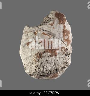 Fragment einer Stuckmaske. Unterer Teil des Gesichts eines bärtigen Mannes; erhalten sind Kinn, Mund, Wangen und ein Teil der Nase. Sarkophag-Maske, 2. Jahrhundert, römische Zeit, Ägypten. Höhe 11,7 cm; Breite 8,7 cm., Ein grob ovaler Stein mit einer rauen, gekörnten Oberfläche sitzt vor einem flachen grauen Hintergrund; der Stein zeigt eine Grundfarbe von hellgrau und cremeweiß mit Flecken und Streifen von rötlich-braunen und kleinen Bereichen von dunklerem Grau bis schwarz gesprenkelt, und seine Oberflächenstruktur umfasst Risse, Grate und ungleichmäßige Einbuchtungen mit einigen Stellen, die glatter und einige weniger körniger aussehen. Stockfoto