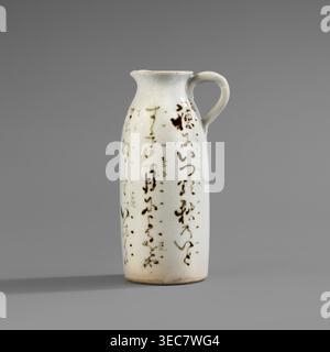 Zylinderförmige Kanne mit kleinem Griff und verbreitertem Auslauf. Weiße Glasur mit feinem Knistern; Deko lackierte Unterglasur mit Eisenoxid schwarz. Inschriften; Japanische Kalligraphie. Keramik, Japanisch; 2. Hälfte des 19. Jahrhunderts. Gefäß, Höhe 11,7 cm, Breite 6,3 cm, Durchmesser 4,7 cm. ein hoher Keramikkrug mit einem schmalen, abgerundeten Körper und einem kleinen gebogenen Griff sitzt auf einem glatten grauen Hintergrund, der Krug in einem blasscremefarbenen weiß glasiert mit einem Netzwerk feiner Knisterlinien, die auf seiner Oberfläche sichtbar sind; über den Körper verteilt sind mehrere unregelmäßige dunkelbraune, pinselartige Flecken und Flecken, die sich bilden Stockfoto