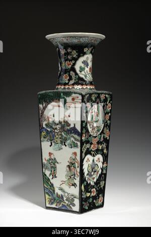 Vase aus der Familie Noire; Chinesisch, Qing-Dynastie Kangxi, 1662–1722; farbiges Porzellan mit gemalten Medaillons mit Schmetterlingen, figurativen Szenen und Pflanzenmotiven; Gefäßvase; Höhe 44,5 cm, Breite 14,2 cm, Tiefe 14,6 cm., Eine hohe, rechteckige Keramikvase mit ausgestelltem Hals sitzt vor dunklem Hintergrund. Die Vase zeigt einen glänzenden schwarzen Hintergrund auf mehreren Gesichtern, dicht verziert mit floralen Motiven in Grün, Rosa, weiß, Orange und blassblau. zusammen mit einigen großen weißen Kartuschenformen, die mit zusätzlichen Blumenmotiven gefüllt sind. Andere Tafeln auf der Vase zeigen ein helles, cremiges Licht Stockfoto