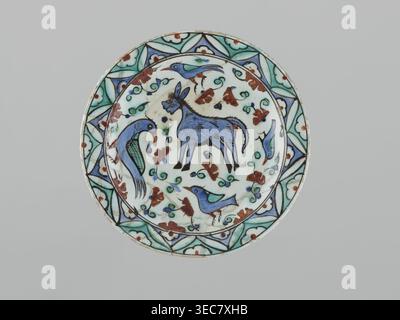 Platte, islamische Kunst, Türkisch, Osmanische Dynastie 1299–1922, Keramik, Iznik, 17. Jahrhundert. Schälgefäß, Höhe 5,3 cm, Durchmesser 26,5 cm, Gewicht 0,62 kg. Dekoration: Im Spiegel ein Esel, vier Vögel und ein Blumenschmuck; am Rand geometrisch-blumig; stilisierte Blumen, Tiere, Vögel, Esel; geometrische und florale Ornamente, Eine runde Keramikplatte mit dekorativem Rand und mittig gemalter Szene, die überwiegend Farben weiß, Blau, Türkis, Grün, Braun, und schwarz; der Rand zeigt sich mit geometrischen und floralen Motiven in Türkis, Grün, Blau und Braun, die in Schwarz gegen A umrissen sind Stockfoto