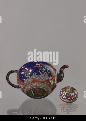 Teekanne kyûsu mit Deckel; Cloisonné Emaille Teekanne, ca. 1906–1908 Meiji 39–41, Kyoto, Japan. Höhe 10,0 cm, Durchmesser 10,0 cm. Auf dem Deckel befindet sich eine stilisierte Lotusblüte. Dekoration: Zwei Reserven auf dem Bauch – ein Pflaumenbaum und ein Vogel – sowie Pflanzen und Schmetterlinge; der Rest des Hintergrunds und das Cover sind mit einer Blumenranke verziert. Themen: Vögel, Pflaumenbäume, Schmetterlinge, Pflanzenmotive., Eine abgerundete Teekanne und ein separater Deckel ruhen auf einer reflektierenden Oberfläche auf einem glatten grauen Hintergrund. Die Teekanne hat eine tiefblaue Oberfläche mit floralen Motiven in Grün, weiß, Gelb und Rot und einem Band von Stockfoto