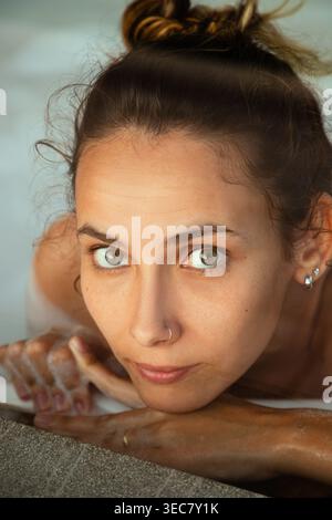 Eine junge Frau nimmt ein Schaumbad und schaut direkt in die Kamera. Sie scheint den Moment zu genießen und scheint sich im warmen Wasser wohl zu fühlen. Blasen s Stockfoto
