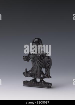 Buddhistischer Mönch, Chinesisch, Qing-Stil, chinesische Kunst, chinesischer Buddhismus, Qing 1644–1911, Luohan Ikonographie, 19. Jahrhundert, China, Skulpturenfigur, Höhe 11,8 cm, Breite 7,1 cm, Tiefe 2,0 cm, Eine glänzend dunkle Figur einer gekleideten Figur steht auf einem kleinen rechteckigen Sockel, die Oberfläche reflektiert Licht und erscheint schwarz mit dezenten Highlights. Die Figur trägt drapierte Kleidungsstücke mit sichtbaren Falten und einen abgerundeten Kopf mit geschnitzten Gesichtszügen. Ein Arm ist nach vorne gestreckt, der andere ist gebeugt und hält einen Teil des Gewandes, und das untere Kleidungsstück zeigt hochgezogene Falten, die die Füße freilegen Stockfoto