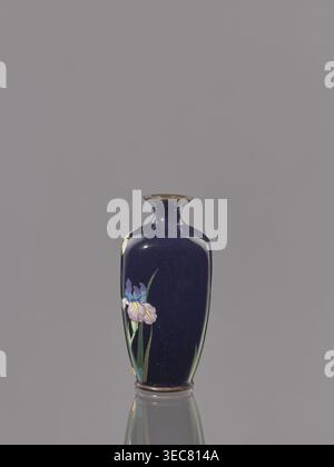 Vase, Geschenk, Iris, Wiederbesitz Krakau, japanische Kunst, Japanisch, Meiji 1868–1912, Cloisonné-Emaille. Eiförmige Vase mit kurzem, dünnem, ausgestelltem Hals; dunkelblauer Hintergrund der Dekoration. CA. 1900 Meiji-Periode, 1868–1912. Japan. Gefäß. Höhe 9,1 cm; Durchmesser 4,3 cm., Eine dunkelblaue Keramikvase mit schmalem Hals und ausgestelltem Rand sitzt mittig auf einem glatten grauen Hintergrund und zeigt glänzende Reflexe; ein Blumenmotiv mit Blütenblättern in violetten, rosa, blauen Tönen und gelben und grünen Blättern ziert eine Seite, und die Basis und der innere Rand der Vase haben subtile bräunliche Töne. Stockfoto
