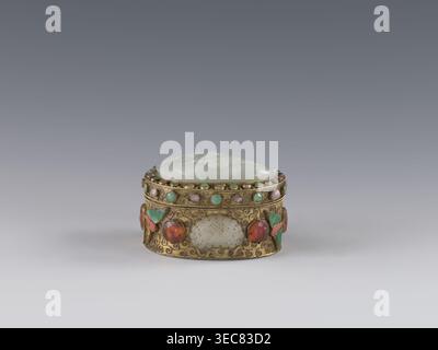 Box mit Deckel, chinesische Kunst, Chinesisch, Qing 1644–1911. Der Deckel ist mit einer Jadeite-Plakette eingelegt, auf der ein Flachreliefbild eines Löwen abgebildet ist, der mit einem Ball spielt. Die äußere Wand zeigt Motive von Schmetterlingen, Fledermäusen und das Shou-Symbol für Langlebigkeit aus Halbedelsteinen in den Kulissen. Hintergrund: Pflanzenzweig mit filigraner Struktur. Ende des 19. Jahrhunderts, China. Behälter/Behälter. Höhe 5,0 cm, Breite 6,6 cm, Tiefe 8,2 cm, Gewicht 0,17 kg., Ein kleiner, verzierter ovaler Kasten sitzt mittig auf einem grauen Hintergrund, mit einem blassgrünen geschnitzten Deckel und einem goldfarbenen Korpus, der mit einigen runden Cabochonsteinen in Grün und verziert ist Stockfoto