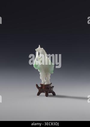 Fischer mit einem Korb und einem Fisch auf einer Rode, unbekannter Bildhauer, Fische, Fischer, chinesische Kunst, chinesische Kultur, Qing 1644–1911, weiße Jade mit grünen Flecken, massive Skulptur, graviert, 19. Jahrhundert, China, Figur, Skulptur, Höhe 7,2 cm, Eine kleine geschnitzte Figur aus durchscheinendem weißem und hellgrünem Material steht auf einem dunkelbraunen Holzsockel; die Schnitzerei hat glatte, fließende Konturen mit unregelmäßigen, abgerundeten Formen und dünnen Vorsprüngen, die Basis ist organisch geformt mit geschwungenen Beinen und einer polierten Oberfläche; der Hintergrund ist ein Verlauf von dunkler Kohle an der Spitze zu hellgrau an der Stockfoto