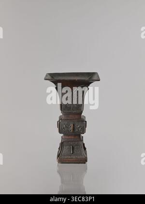 Fangzun Vase, chinesische Kunst, chinesische Kultur, Pflanzenschmuck, Bananenpflanzen, Mäanderschmuck, Taotie-Ikonographie, zeremonielles Gefäß, Ritualgefäß, Qing-Dynastie 1644–1911, Qing-Stil, 19. Jahrhundert, China Ausgabeort?, Schiff; Höhe 21,4 cm, Breite 13,3 cm, ein Ständer, dunkelbraunes und schwarz geschnitztes Objekt mit einer ausgestellten quadratischen Oberseite und einer abgestuften quadratischen Basis, das kunstvoll geschnitzte Paneele und sich wiederholende geometrische und geschwungene Motive an den Seiten zeigt, steht auf einer reflektierenden hellgrauen Oberfläche vor einem hellgrauen Hintergrund, das Objekt bildet eine weiche Reflexion darunter. Stockfoto