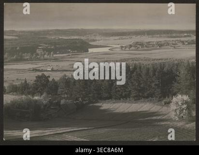 Der Neris Fluss in Ponary; Fotograf Jan Bułhak 1876–1950; Vilnius, ca. 1934; Fotografie der Natur, 11,5 x 16,2 cm; Thema: Die Flüsse Neris, Landschaften; Rolle des Fotografen/Klassifizierung notiert; Provenienz: Kauf; Inschrift/Verein: Orłowicz, Mieczysław 1881–1959 erwähnt., Eine weite Luftaufnahme einer ländlichen Landschaft mit einem Vordergrund von bewirtschafteten Feldern mit sichtbaren Furchen, einer Gruppe dunklerer Bäume, die einen dichten Stand in der Mitte bilden, und einigen verstreuten Gebäuden mit geneigten Dächern in der Nähe der Baumgrenze; hinter den Bäumen sind offene Felder und Wiesen mit heller Farbe Stockfoto