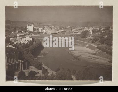 Wilia auf dem Weg zur Grünen Brücke; Foto, Wilno Album, Band 1; Jan Bułhak 1876–1950; Vilnius Panoramen; Wilia Fluss, Panorama von Vilnius; 1912; Foto, Fotodruck: 11,0 x 16,0 cm; Albumseite: 31,0 x 23,5 cm, das Bild zeigt eine urbane Szene am Fluss mit einem breiten Fluss, der durch das Zentrum schwingt, umgeben von baumgesäumten Böschungen und Sandbänken. Am nahen Ufer befindet sich eine Promenade mit ein paar Bäumen und ein großes Gebäude mit Bögen und Balkon. Auf der anderen Seite des Flusses erhebt sich eine Gruppe von Gebäuden auf sanft geschwungenem Land, darunter eine prominente zweitürmige Kirche mit einem Stockfoto