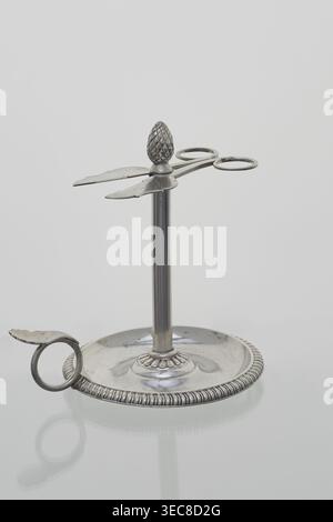 Scherenförmiger Kerzenhalter stoczek, Jan Radecki fl. 1815–1837, Goldschmied. Kerzenhalter für eine dünne Kerze, die sich um den Stiel dreht; auf einer plattenförmigen Basis mit einem Halbzylinder abgestützt; mit einem Griff in Form eines Rings mit Daumenauflage versehen. Der Stiel ist eine Hülse, um die die dünne Kerze gedreht wird; die Hülse wird mit einem Kiefernzapfen und einem Schraubstock in Form einer flachen Schere mit Spiralgriffen versehen, um die Kerze auf die gewünschte Länge zu verlängern. 1815–1837, Poznań, Polen. Funktion: Beleuchtung. Abmessungen: Höhe 14,5 cm, Breite 14 cm, Tiefe 11 cm, Ein metallisches Objekt mit einem Stockfoto