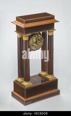 Manteluhr von Alexandre Pertrand fl. CA. 1840. Manduhr in Form eines viersäuligen Portikus auf Quader- und Gegenfuß; Buchsholzeinlagen auf der Vorderseite des Gesimses und des Sockels mit einer Rhombenrosette und einer Ranke auf beiden Stielen; vergoldete Bronzeböden und Kapitelle. Zwischen den Säulen hängt ein Hängewerk mit silbernem Zifferblatt mit römischen Ziffern und zwei Schlüssellöchern. Vergoldeter Bronzahmen mit Muscheln umgibt die Uhr. Eichenkonstruktion mit Palisander und hellen Holzeinsätzen. Ca. 1840, Paris, Frankreich. Uhr. Höhe 47 cm, Breite 21 cm, Eine freistehende Holzkonstruktion mit einem Stockfoto
