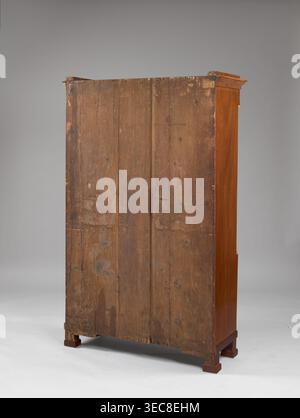 Bibliotheksschrank, Empire-Stil, Pfeile, Säulen, Plattenschmuck, Vorkriegszeit, 1. Viertel des 19. Jahrhunderts, Warschau, Möbel, Lagermöbel; Höhe 169 cm, Breite 107 cm, Tiefe 40 cm., Ein hoher Holzschrank von hinten betrachtet, der eine große vertikale Holzplatte mit sichtbarer Körnung, Knoten, Kratzern und abgenutzten Bereichen in Brauntönen zeigt, gestützt von einem Sockel mit blockigen Füßen in dunklerem Braun; die rechte Seite des Schranks zeigt eine glattere, polierte Holzoberfläche in warmem Rotbraun, und die obere Kante hat eine kleine überhängende Form in ähnlichem Rotbraun; der Hintergrund ist glattes neutrales Grau Stockfoto