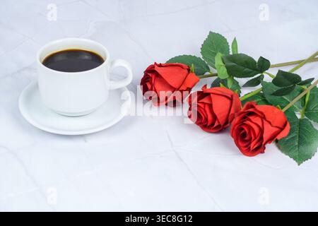 Weiße Tasse schwarzen Kaffee neben roten Rosen auf hellem Marmor, romantische ruhige Szene für Geschenke, Intimität und Lebensstil. Stockfoto