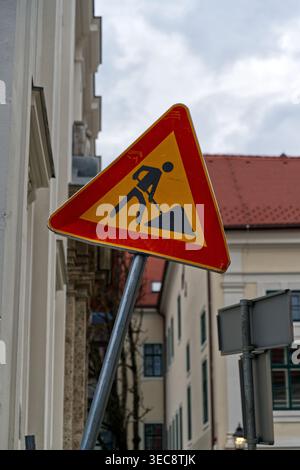 Ein dreieckiges Warnschild für die Baustelle mit rotem Rand und gelbem Hintergrund steht in einer städtischen Umgebung Stockfoto